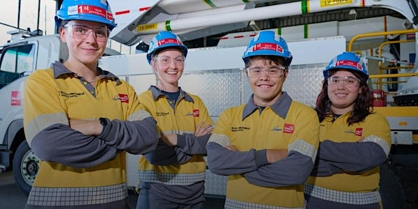 Four people in hard hats and hi vis clothing smiling in front of a truck in a large garage